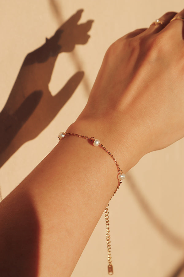 Close-up of a womans wrist wearing an adjustable pearl bracelet with a gold chain, emphasizing the bracelet's refined design and subtle sophistication.