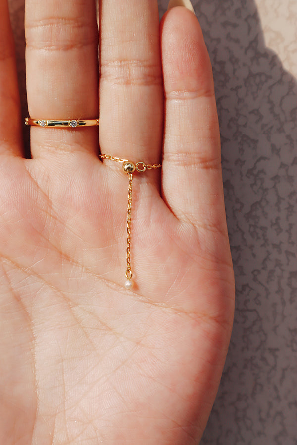 Close-up of a hand wearing a delicate pearl chain ring, showcasing the adjustable gold chain at the back of the ring.