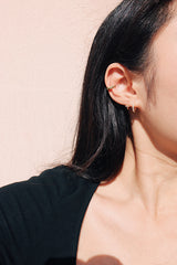 Model in black with dainty gold earrings stacks standing under the sun
