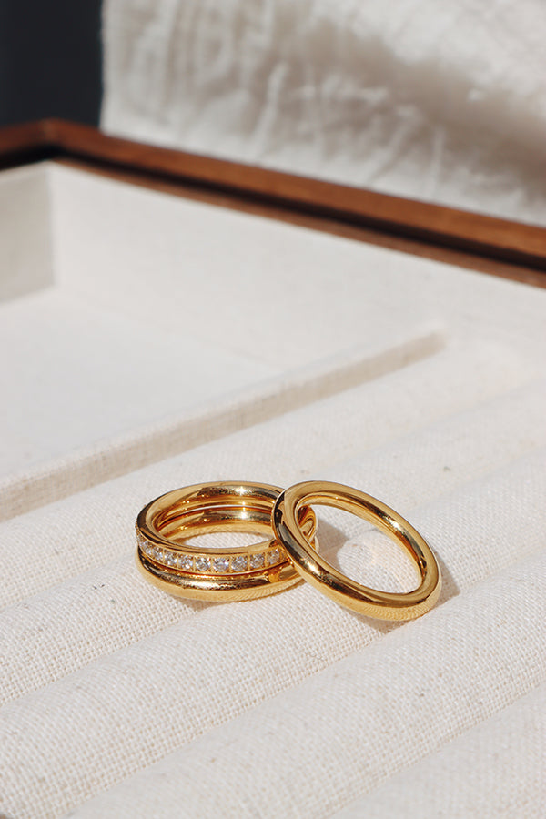 Close-up of two gold stacking rings, one plain and one with zirconia accents, placed in a soft beige jewelry tray, emphasizing their sleek and refined design by shnco.