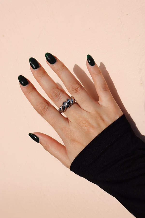 Hand wearing a silver croissant ring casting a subtle shadow on a pastel beige wall.