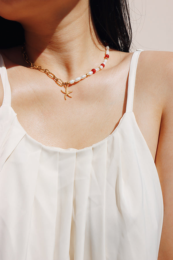 A womans neck styled with a choker featuring a gold chain, freshwater pearls, and red agate beads, designed with a central starfish pendant, capturing the beach-inspired aesthetic of SH & Co. Jewelry.