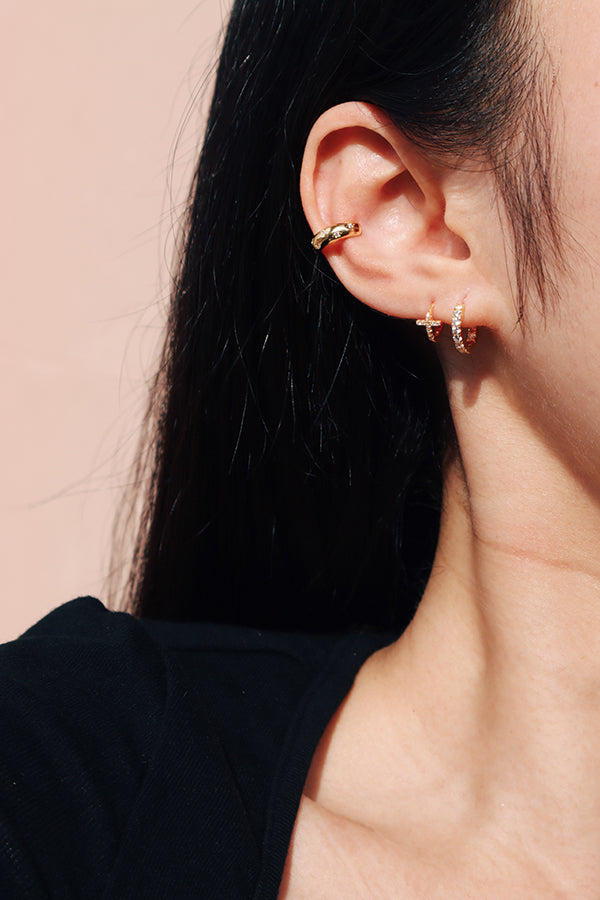 Asian woman stacks gold earring studs and ear clip on her right ear