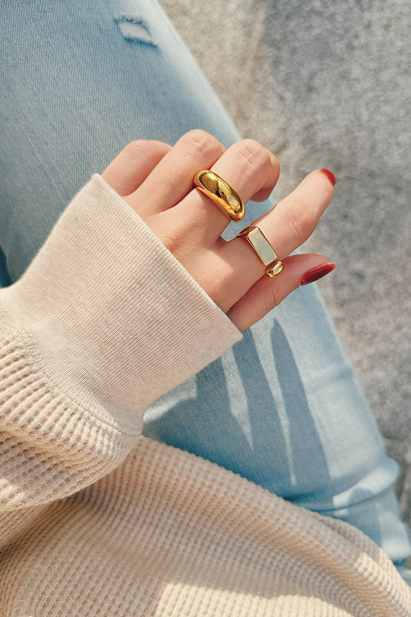 Hand wearing gold chunky rings with a cozy beige sweater and light wash jeans, capturing a casual and stylish vibe in natural sunlight.