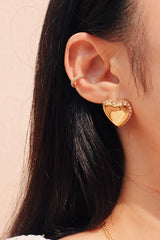 Girl wearing gold heart shape earring with zirconia stacked with a zirconia ear clip under the sun