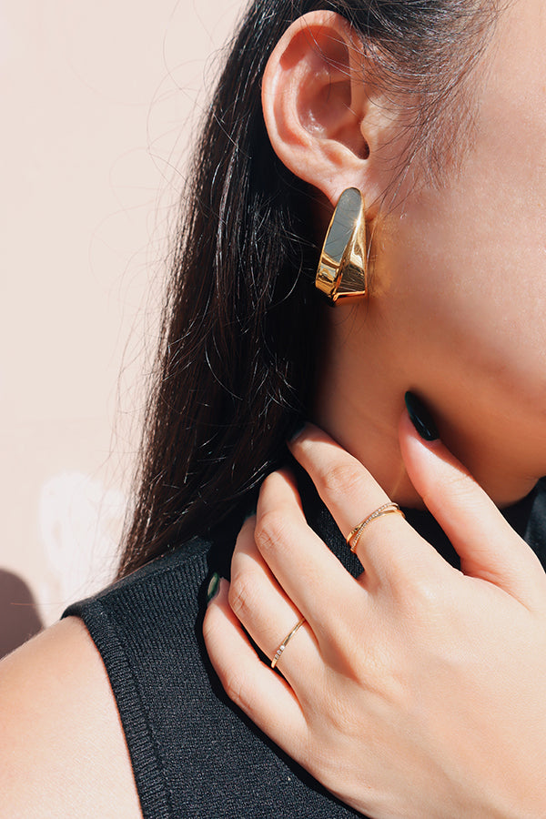 Close-up shot of a woman wearing bold gold hook earrings and minimalist gold rings, pairing with a sleeveless black top under direct sunlight.