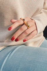 Close-up of a hand wearing two gold statement rings paired with a cozy knit sweater and blue jeans, showcasing modern, minimalistic jewelry styling.