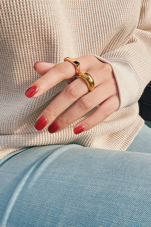 Close-up of a hand wearing two gold statement rings paired with a cozy knit sweater and blue jeans, showcasing modern, minimalistic jewelry styling.