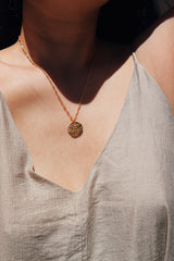 A close-up of a woman wearing a gold hand of Fatima pendant necklace, layered with a pearl choker, captured in natural light to emphasize the detailed craftsmanship of the jewelry.