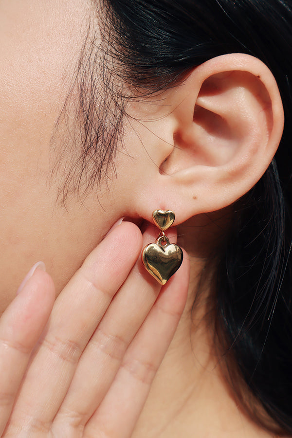 Girl from shnco using her hand to direct the attention to her ear wearing heart shape gold earring on one side