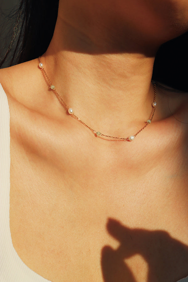 A minimalist design of a jade and pearl choker necklace, hypoallergenic and gentle on the skin, worn by a woman in a well-lit close-up image.