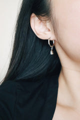 Close-up of a silver drop earring with a single crystal teardrop hanging, elegantly worn by a woman with long black hair. The earring adds a touch of sophistication to her minimal style.