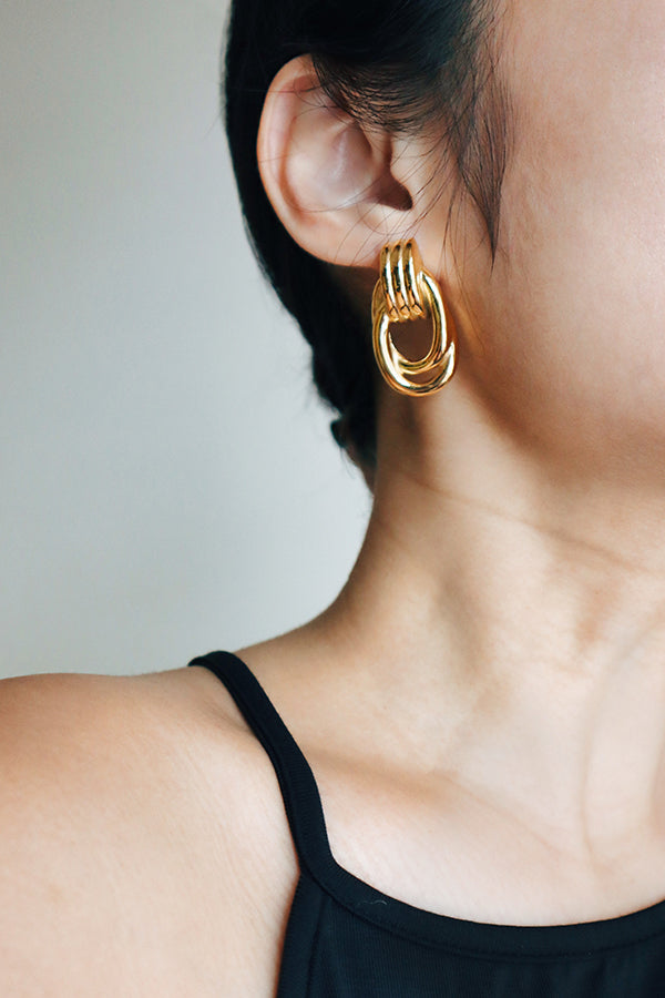 Close-up of a person wearing a bold, layered gold earring, styled with a black sleeveless top.