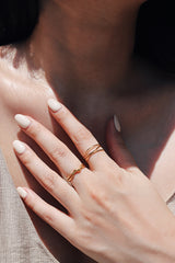 Close-up of a womans hand wearing a matching Griselda crossed gold ring, paired with another gold ring, showcasing the rings chic and versatile style.