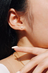 Close-up of a woman's ear showcasing a freshwater pearl earring, styled with a layered gold necklace featuring small pearls.