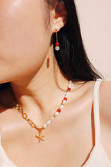 A stylish choker made of red agate and freshwater pearls with a gold starfish pendant, elegantly worn by a woman, showcasing the choker's detailed craftsmanship.