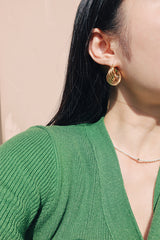 Girl wearing a green cardigan with medium size textured gold hoops along with a pearl necklace in sunlight