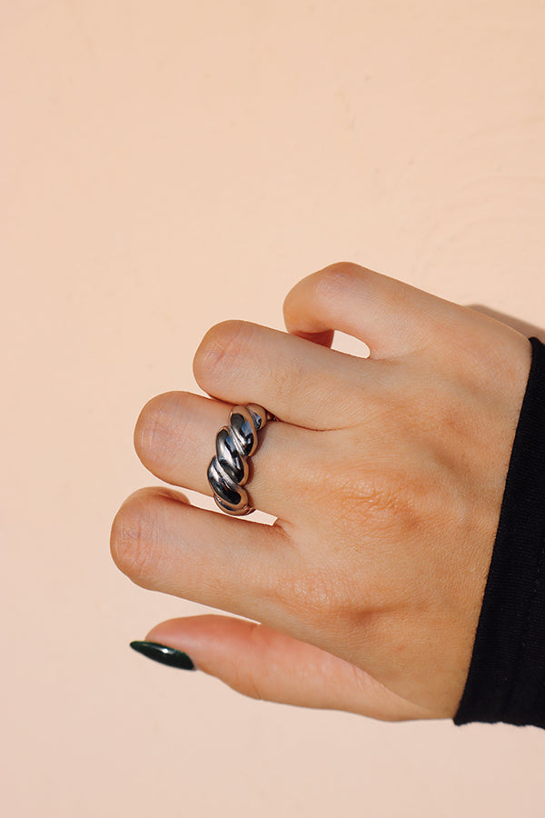 Silver croissant ring adorning a hand with forest green nails, the background in soft pastel beige highlights the ring’s vibrant gold color.