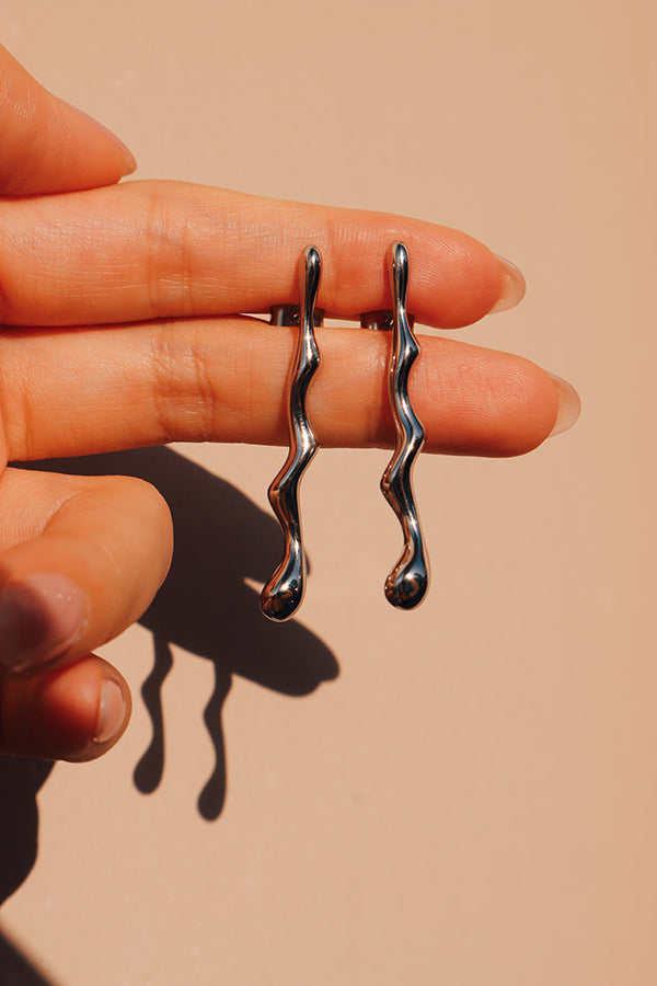A pair or silver drop earrings held in hand under the sun