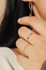 A close-up view of a hand wearing a stacking pearl chain ring with a 14K gold-plated band, capturing the shimmer of the ring under sunlight.