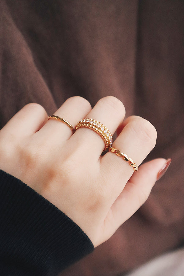 A close-up shot of a hand adorned with three layered gold rings, highlighting their intricate details and minimalist yet elegant design.