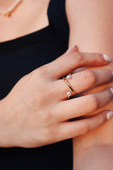 Close-up of a woman's hand wearing a twisted gold pearl ring, capturing the ring's elegant and minimalist design against a neutral background.