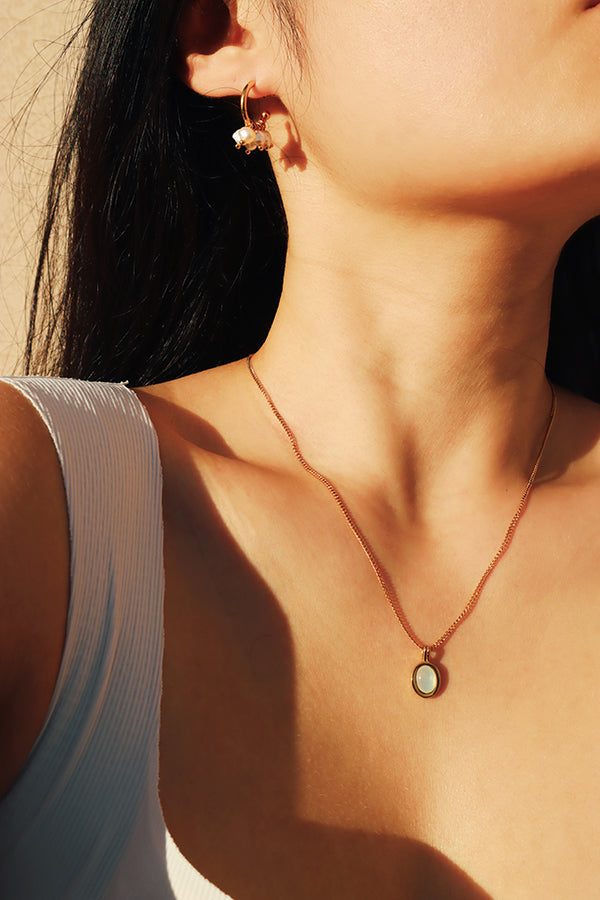 Close-up of a woman wearing unique gold pearl hoop earrings and a delicate pendant necklace, showcasing the earrings luxurious style against a warm sunlight background.