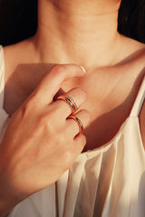 Womans hand gently placed near her neckline, adorned with a gold stacking ring set, including one with sparkling zirconia, displaying the rings stylish and sophisticated appeal.