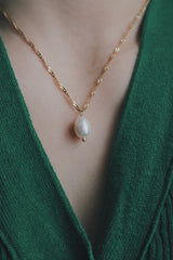 Close-up of a woman wearing an 18K gold necklace featuring a freshwater pearl pendant, styled with a green knit top, showcasing the necklaces elegant and timeless design.