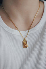 Close-up of a woman wearing the 18K gold-plated Phoebe Luna necklace with an engraved crescent moon pendant, styled with a white ribbed top, showcasing the necklace's intricate design.