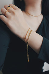 A womans wrist adorned with an 18K gold-plated rope chain bracelet, styled alongside another gold bracelet and rings, highlighting a sophisticated and layered look.