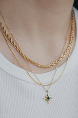 Layered 18K gold necklaces featuring a star pendant with a green cubic zirconia, worn with a white top.