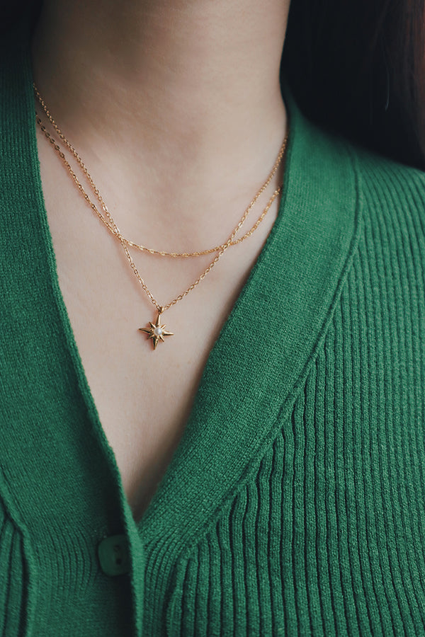 Delicate 18K gold star necklace with a pearl center, styled with a green knit top.