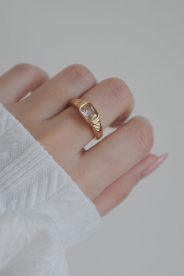 A detailed image of a womans hand adorned with a gold-plated ring featuring a clear cubic zirconia stone. The rings sleek and classic design makes it ideal for stacking with other rings or as a delicate standalone accessory.