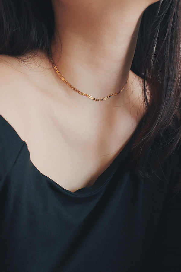 Close-up of a delicate 18K gold-plated choker on a womans neck, showcasing a subtle twist design against a dark blouse.