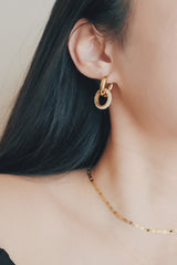 A close-up shot of a woman wearing gold hoop earrings with a circular cubic zirconia-encrusted charm. The earrings feature a modern twist on the traditional hoop design, offering a mix of elegance and contemporary style.