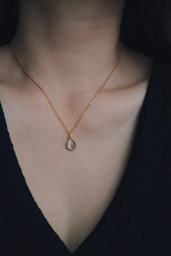 Close-up of a woman wearing a dainty gold-plated necklace with a teardrop-shaped cats eye gemstone pendant, styled with a black textured V-neck top, perfect for wedding outfits.