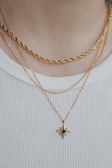 Layered 18K gold star necklaces featuring a green cubic zirconia center, worn with a white top.