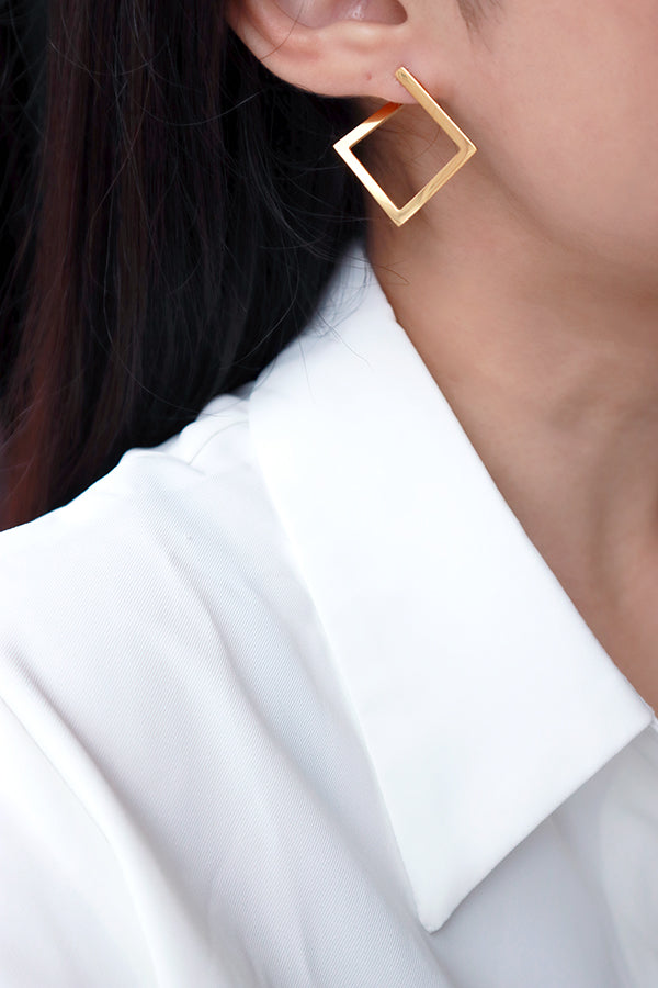 Woman in white shirt wearing SH&Co. square gold hoops