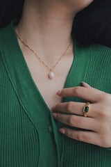 A woman wearing a gold-plated necklace with a single freshwater pearl pendant, paired with a green knit cardigan, highlighting the necklace's classic and sophisticated look.