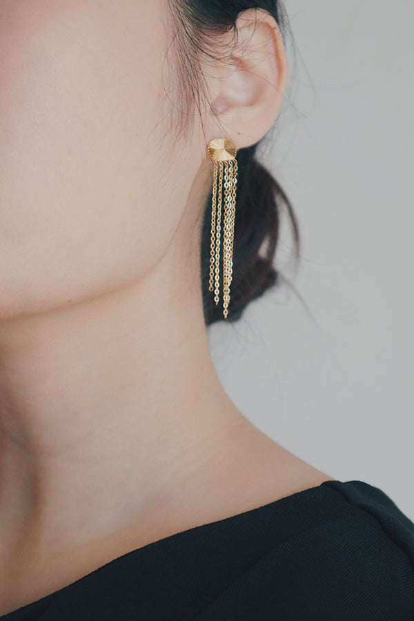 A product image of gold tassel earrings, displayed flat to emphasize their intricate design. The earrings are adorned with a sunburst motif on the stud and long gold chains that dangle gracefully, perfect for adding a touch of elegance to any outfit.