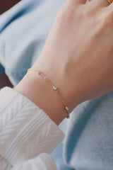 Close-up of a wrist wearing a hypoallergenic gold bracelet adorned with cubic zirconia stones, paired with a gold ring, and styled with a white sweater and light blue jeans.