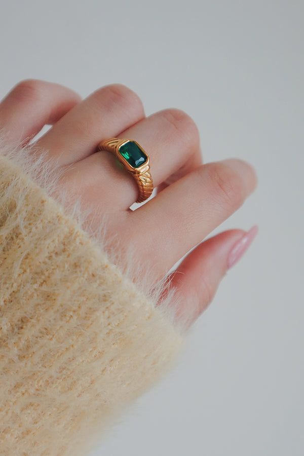 A close-up image of a gold ring featuring a green cubic zirconia stone. The rings vibrant green stone and vintage-inspired band design offer a unique and eye-catching accessory, perfect for adding a pop of color to your jewelry collection.