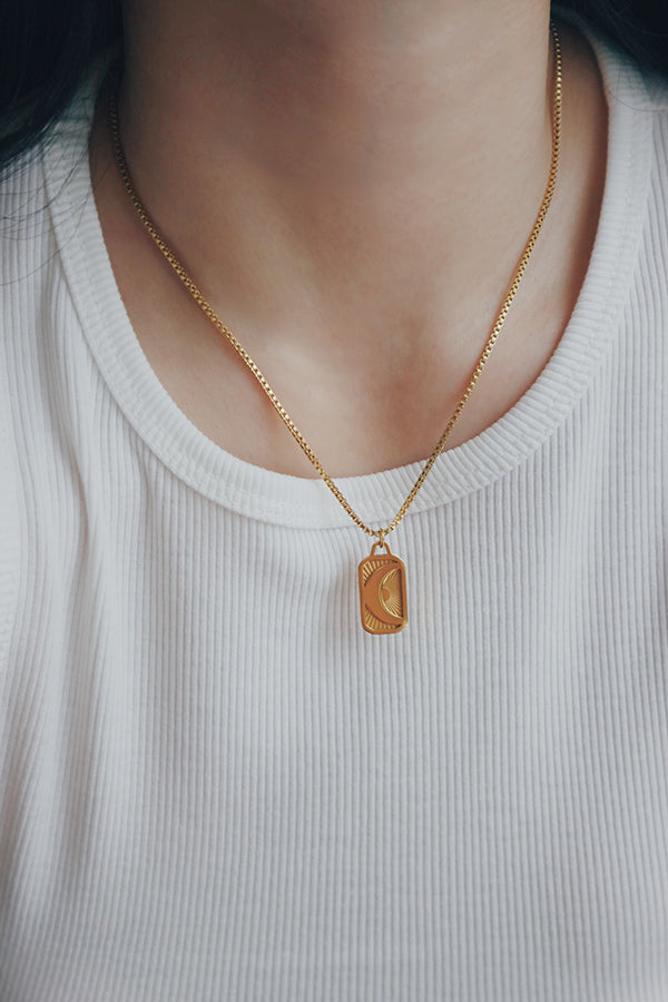 Close-up of a woman wearing a hypoallergenic Phoebe Luna necklace featuring a gold-plated pendant with an engraved crescent moon and sunburst design, styled with a white ribbed top.