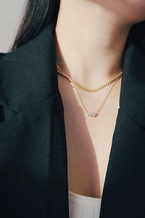 Layered gold necklaces featuring a rope chain and a dainty cubic zirconia pendant, styled with a black blazer over a white top, highlighting the hypoallergenic rope chain necklace.