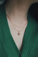 Hypoallergenic gold star necklace with a pearl center, styled with a green knit top.