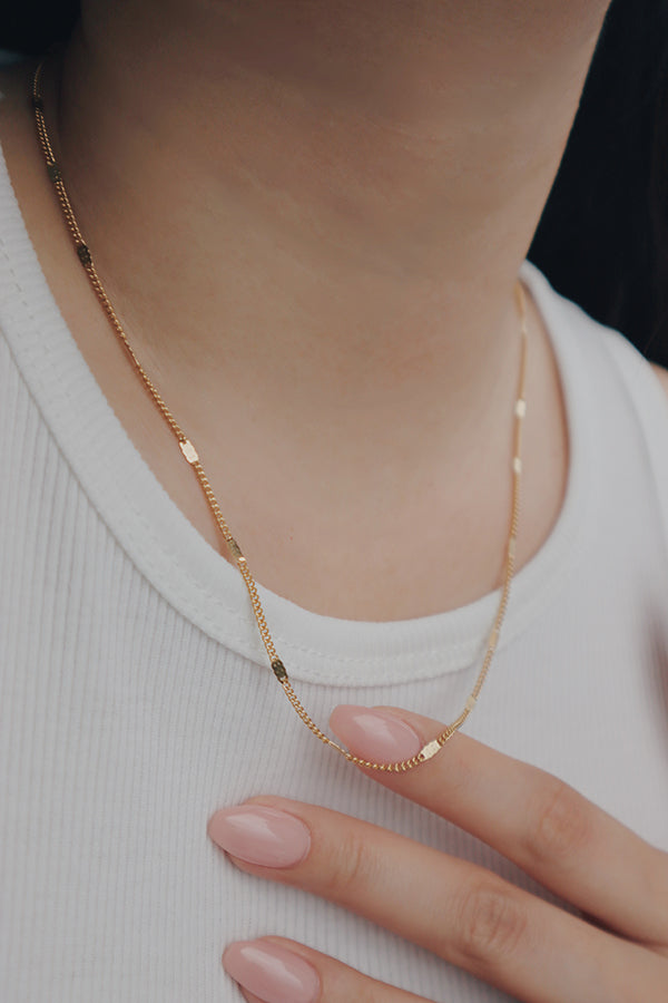 A woman models an essential layering gold necklace by SH & Co., perfect for combining with other pieces.