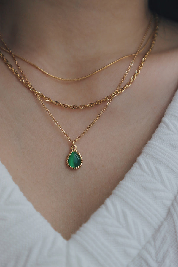 A layered necklace set featuring a dainty gold chain with a teardrop cat's eye pendant and a delicate chain with cubic zirconia stones, worn with a black V-neck top.