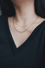 A woman stylishly wears a set of SH & Co. gold necklaces, layered to showcase their unique chain styles and textures.