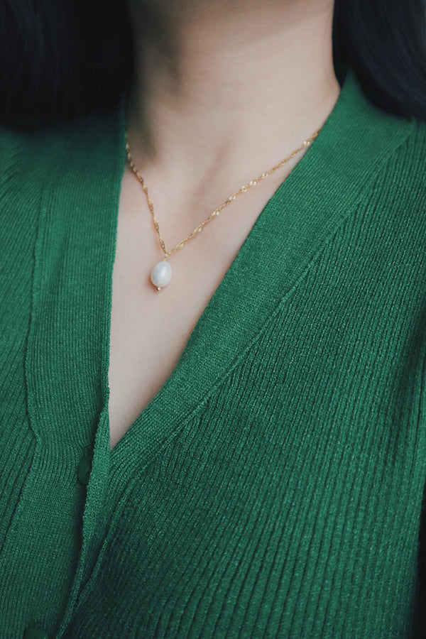 Close-up of a woman wearing the Maeve freshwater pearl necklace with a gold-plated chain, styled with a green knit top, focusing on the necklace's luxurious and refined appearance.